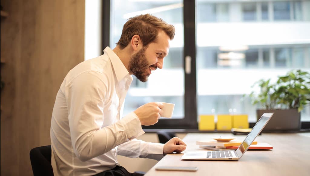 uploads - Jornal_das_Oficinas_EstudoPSE_man-holding-teacup-infront-of-laptop-on-top-of-table-inside-925786